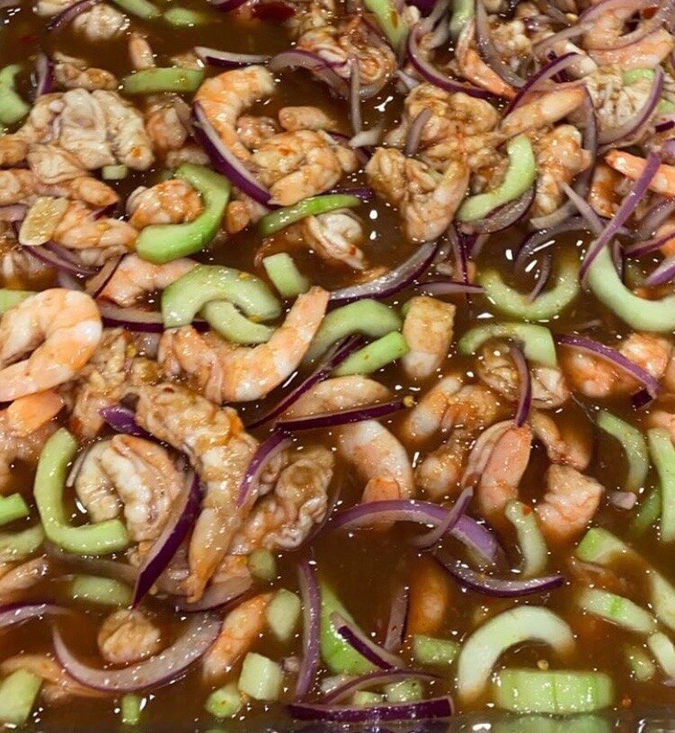 Shrimp aguachile negro in a tray with sliced cucumber and red onion in dark salsa negra