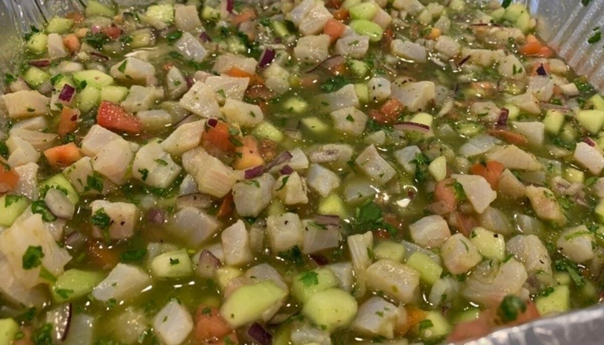 Fish ceviche curing in a tray with diced tomato, cucumber, red onion and cilantro in fresh lime juice