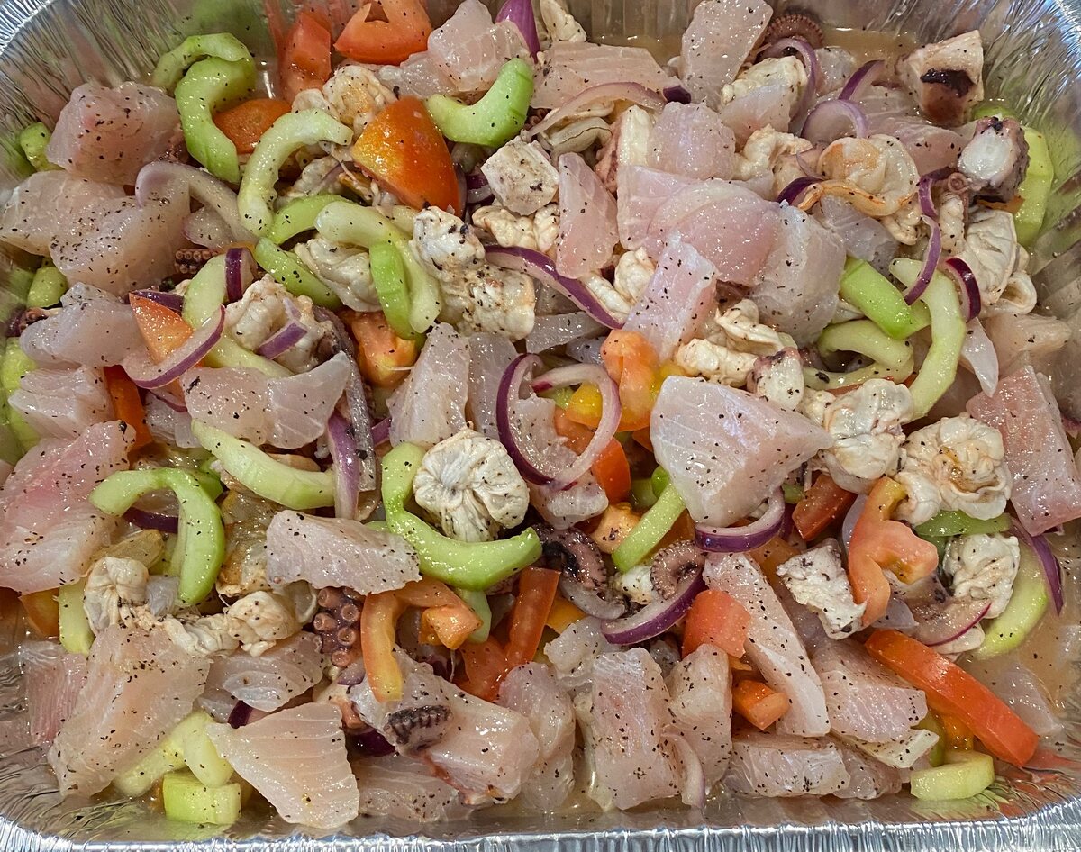 A catering tray of shrimp, fish and octopus ceviche with cucumber, tomato and red onion