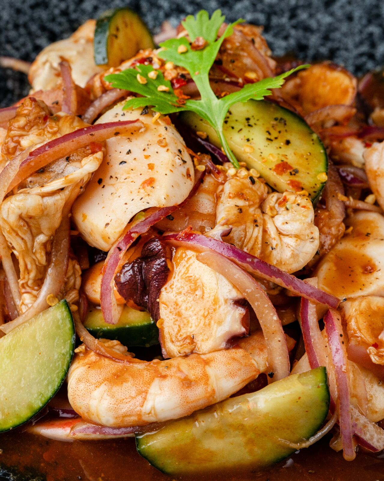 Close-up of shrimp, octopus, cucumber and red onion in a dark salsa inside a stone molcajete