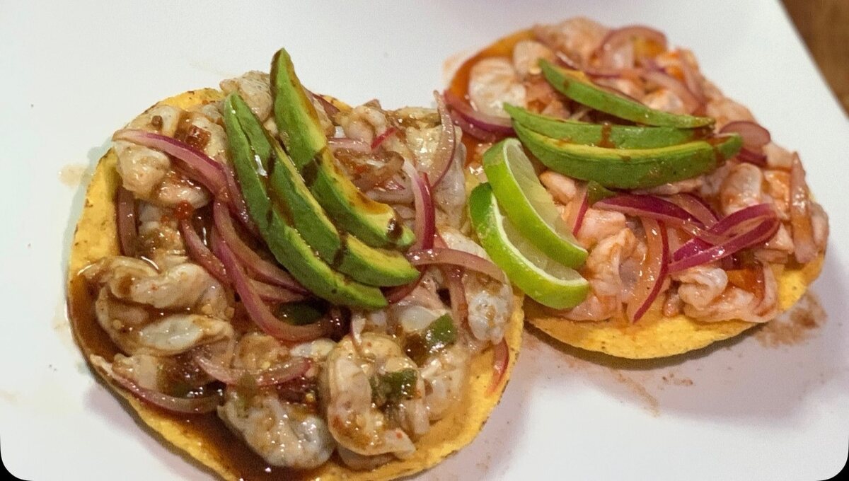 Two shrimp ceviche tostadas topped with avocado, red onion and lime